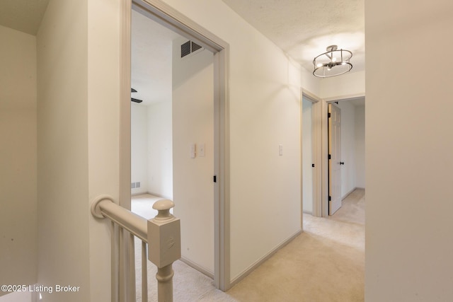 hallway featuring light colored carpet, visible vents, baseboards, and a textured ceiling