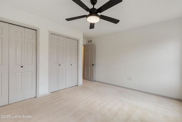 unfurnished bedroom featuring light carpet, baseboards, visible vents, ceiling fan, and multiple closets