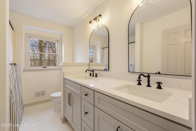 bathroom with visible vents, a sink, toilet, and double vanity