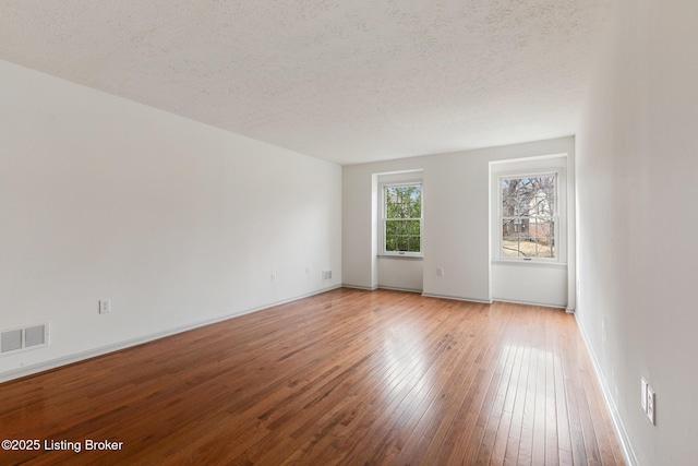 unfurnished room featuring light wood-type flooring, baseboards, visible vents, and a textured ceiling