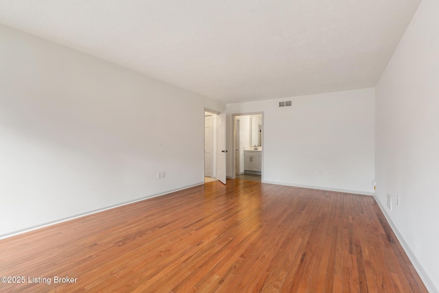 unfurnished room with wood finished floors, visible vents, and baseboards