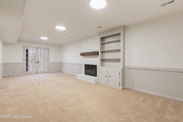 unfurnished living room featuring light carpet, visible vents, wainscoting, french doors, and a fireplace