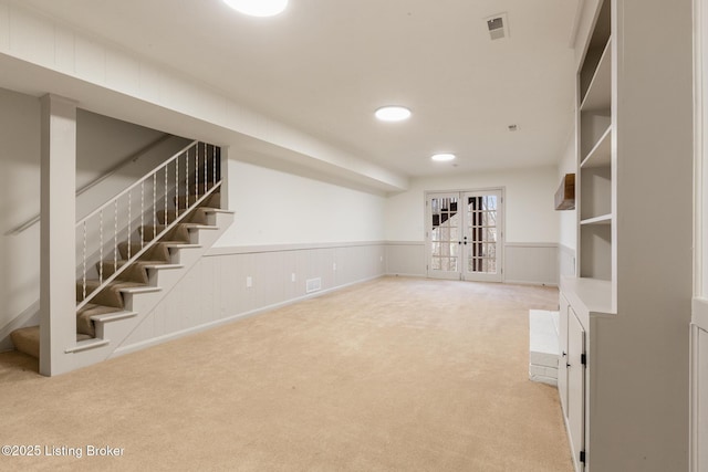 below grade area with light carpet, a wainscoted wall, visible vents, and stairway