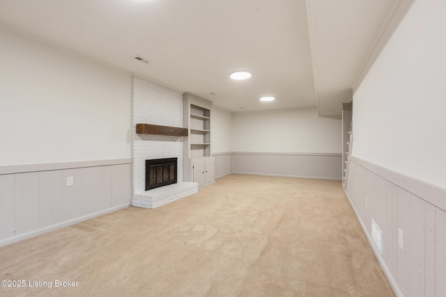 unfurnished living room with a wainscoted wall, visible vents, a brick fireplace, and light carpet