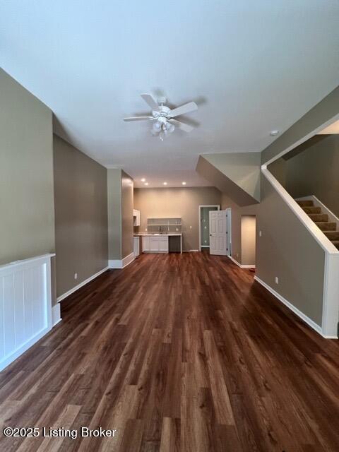 unfurnished living room featuring dark wood-style flooring, stairway, a ceiling fan, and baseboards