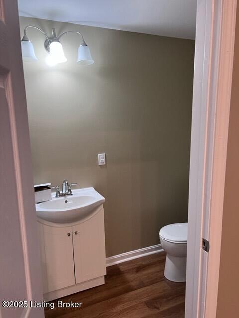 half bathroom with baseboards, vanity, toilet, and wood finished floors