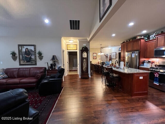 kitchen with appliances with stainless steel finishes, a center island with sink, a kitchen bar, dark hardwood / wood-style flooring, and decorative light fixtures