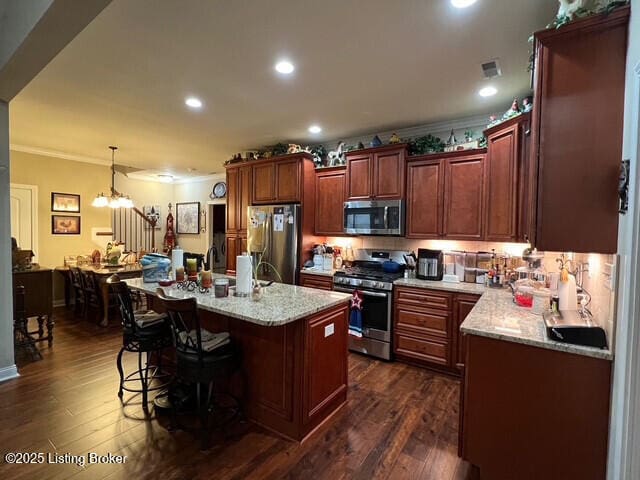 kitchen with light stone counters, dark hardwood / wood-style floors, pendant lighting, stainless steel appliances, and a kitchen island with sink