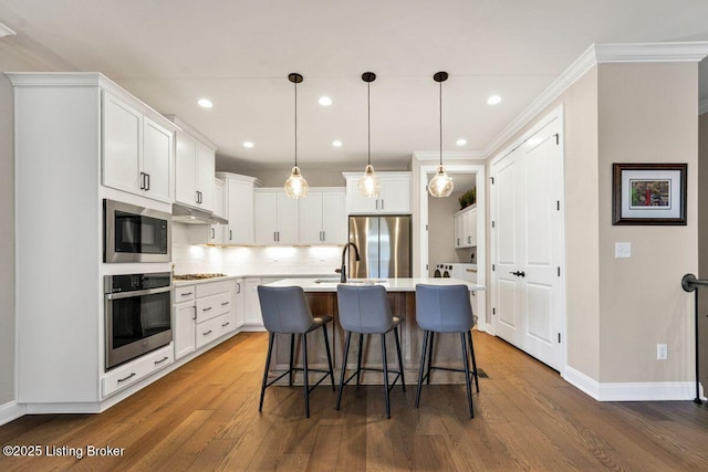 kitchen featuring under cabinet range hood, a kitchen bar, light countertops, white cabinets, and stainless steel appliances