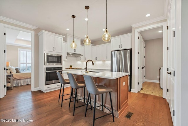 kitchen with visible vents, a sink, under cabinet range hood, wood finished floors, and stainless steel appliances