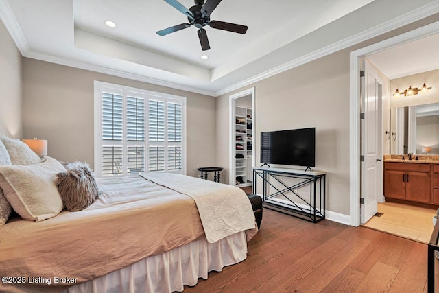 bedroom featuring a sink, light wood-style flooring, a tray ceiling, and ornamental molding