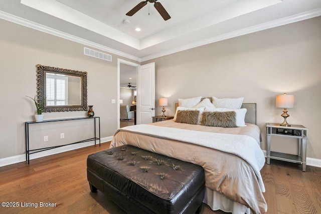 bedroom with visible vents, a tray ceiling, wood finished floors, crown molding, and baseboards