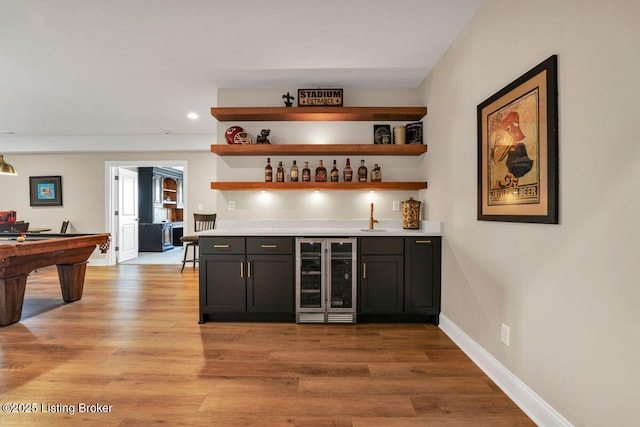 bar featuring wine cooler, indoor wet bar, light wood-type flooring, and baseboards