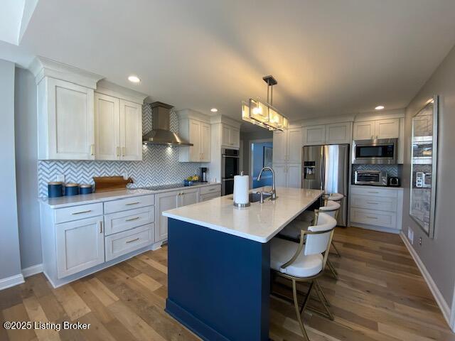 kitchen featuring white cabinetry, wall chimney range hood, pendant lighting, and appliances with stainless steel finishes