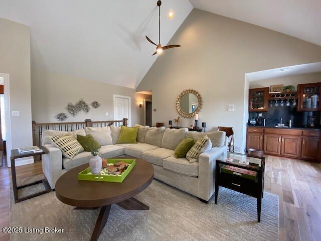 living room featuring wet bar, high vaulted ceiling, light hardwood / wood-style floors, and ceiling fan