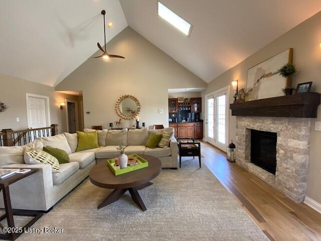 living room featuring a stone fireplace, high vaulted ceiling, and light wood-type flooring