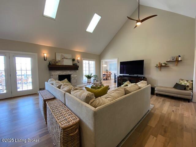 living room featuring ceiling fan, high vaulted ceiling, a stone fireplace, and light hardwood / wood-style floors