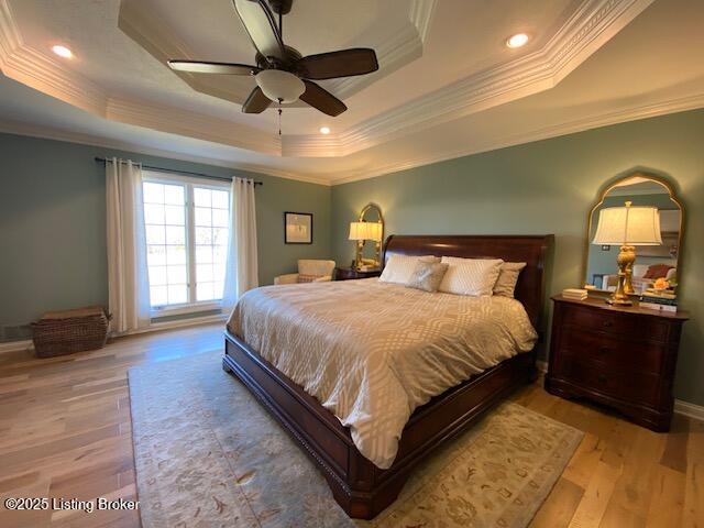 bedroom with ornamental molding, a raised ceiling, and light hardwood / wood-style flooring