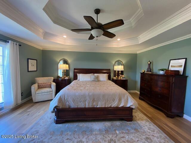 bedroom with ceiling fan, ornamental molding, a tray ceiling, and light wood-type flooring