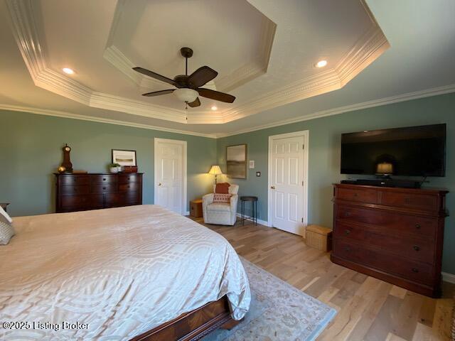 bedroom with crown molding, a tray ceiling, light hardwood / wood-style floors, and ceiling fan