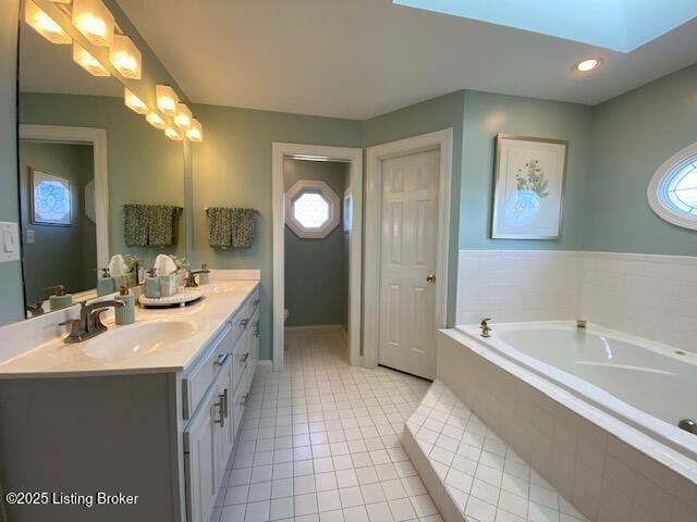 bathroom featuring a skylight, tile patterned flooring, vanity, a relaxing tiled tub, and toilet