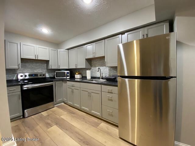 kitchen featuring tasteful backsplash, stainless steel appliances, sink, and light wood-type flooring