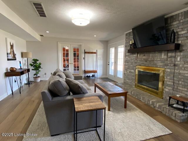 living room with a brick fireplace, french doors, a textured ceiling, and light wood-type flooring