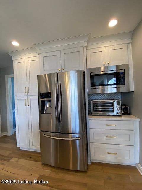 kitchen featuring white cabinetry, decorative backsplash, stainless steel appliances, and light hardwood / wood-style floors