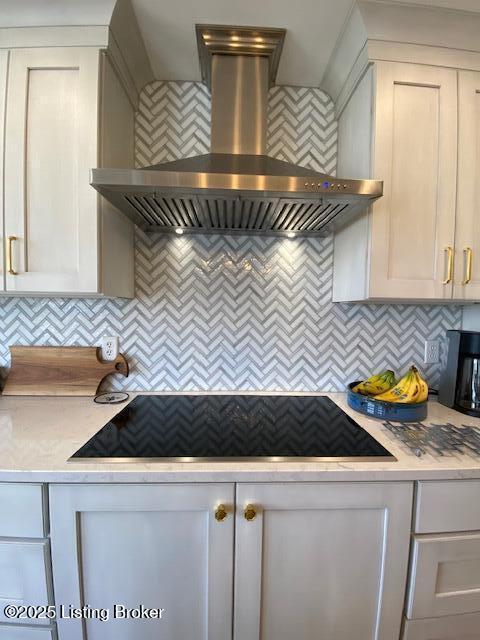 kitchen with backsplash, white cabinets, range hood, and black cooktop