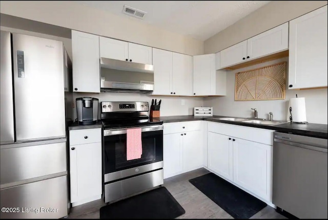 kitchen with appliances with stainless steel finishes, sink, white cabinets, and light wood-type flooring