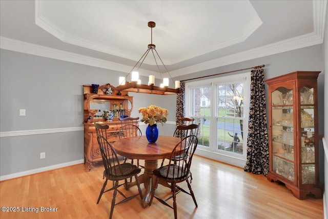 dining room with crown molding, a tray ceiling, a chandelier, and light hardwood / wood-style flooring