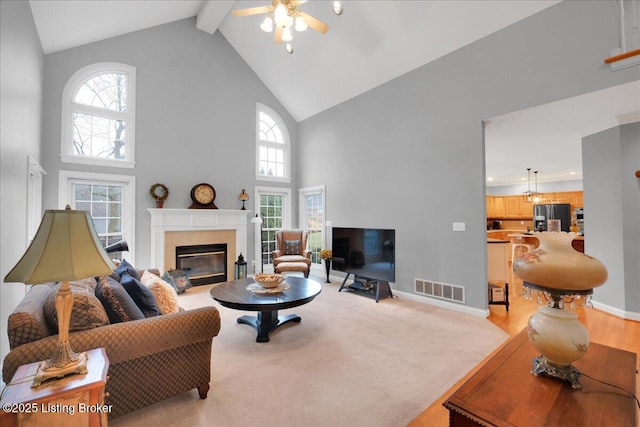 living room with beamed ceiling, plenty of natural light, high vaulted ceiling, and light carpet