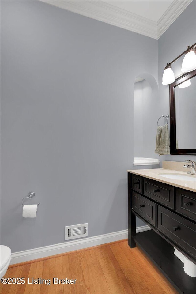 bathroom with hardwood / wood-style flooring, ornamental molding, vanity, and toilet