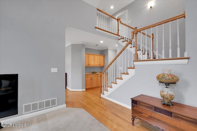 stairs featuring hardwood / wood-style flooring, ornamental molding, and a high ceiling