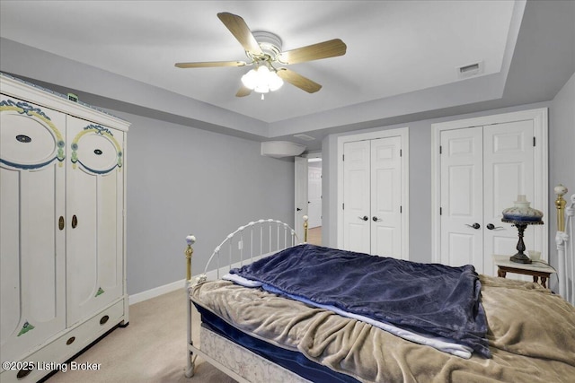 bedroom featuring multiple closets, light colored carpet, and ceiling fan