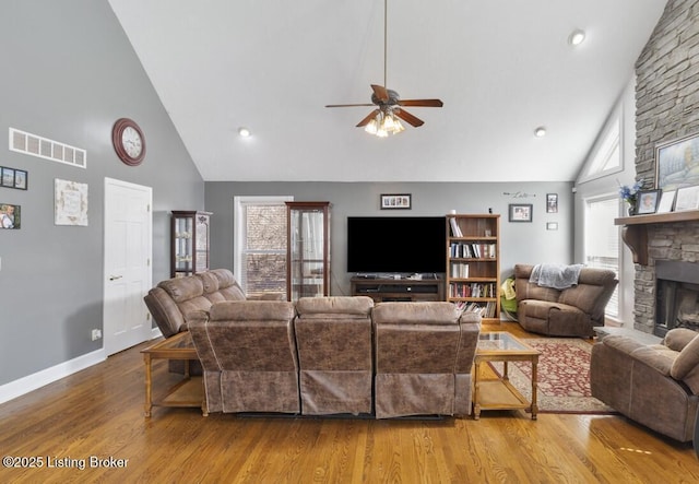 living room with visible vents, a ceiling fan, wood finished floors, a stone fireplace, and high vaulted ceiling