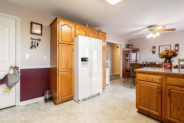 kitchen with a textured ceiling, white refrigerator with ice dispenser, and ceiling fan