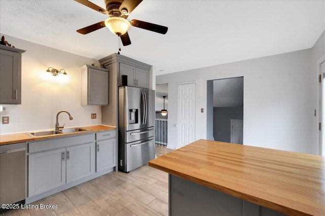 kitchen with gray cabinets, appliances with stainless steel finishes, butcher block countertops, sink, and light hardwood / wood-style flooring