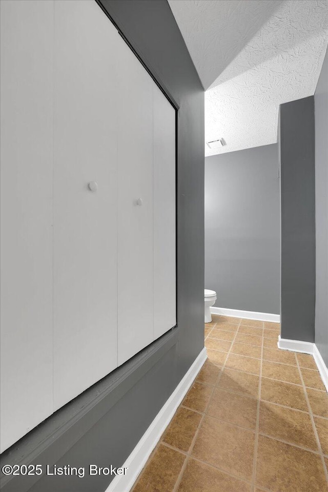 bathroom featuring toilet, tile patterned flooring, and a textured ceiling