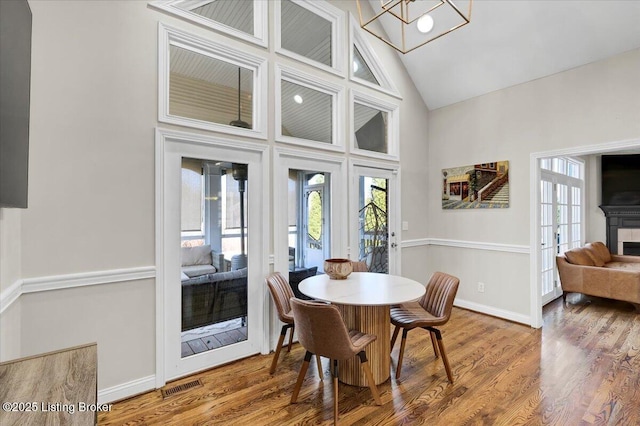 dining area with french doors, high vaulted ceiling, hardwood / wood-style floors, and a tile fireplace