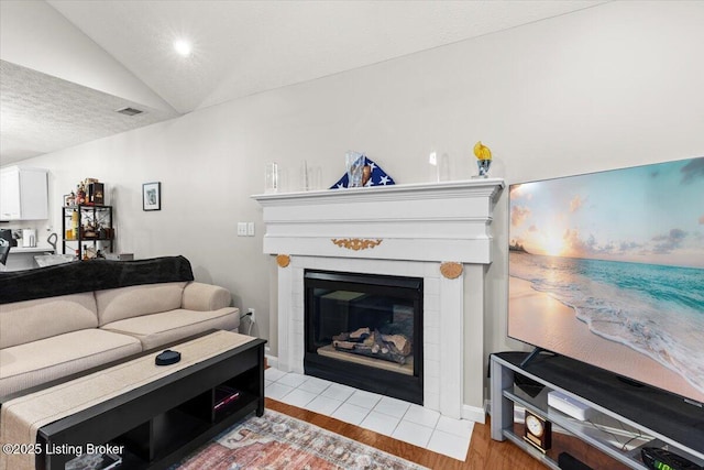 living room with vaulted ceiling, light hardwood / wood-style floors, a tile fireplace, and a textured ceiling