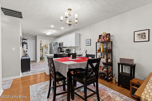 dining room with wood-type flooring, a textured ceiling, and an inviting chandelier