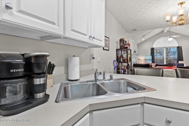 kitchen with sink, lofted ceiling with beams, a textured ceiling, ceiling fan with notable chandelier, and white cabinets