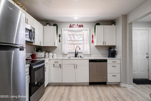 kitchen with light wood-type flooring, appliances with stainless steel finishes, white cabinets, and a sink