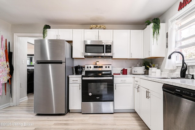 kitchen with white cabinetry, stainless steel appliances, a sink, and light countertops