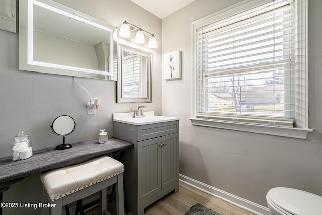 half bath with toilet, vanity, baseboards, and wood finished floors