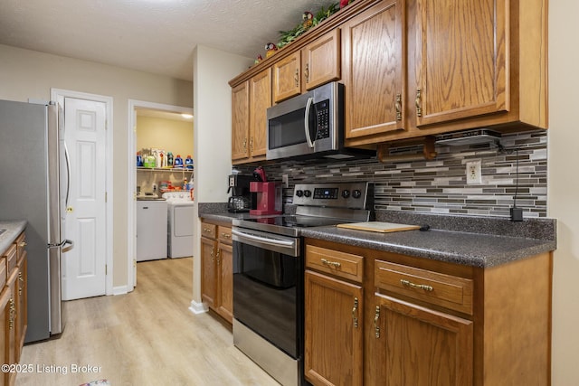 kitchen featuring washer and dryer, tasteful backsplash, stainless steel appliances, a textured ceiling, and light hardwood / wood-style flooring