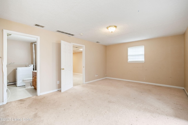 unfurnished bedroom featuring light carpet, connected bathroom, and a textured ceiling