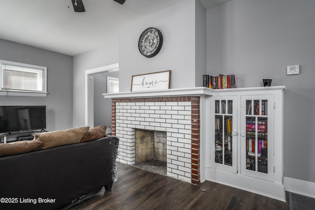 living room with a brick fireplace, dark hardwood / wood-style floors, and ceiling fan