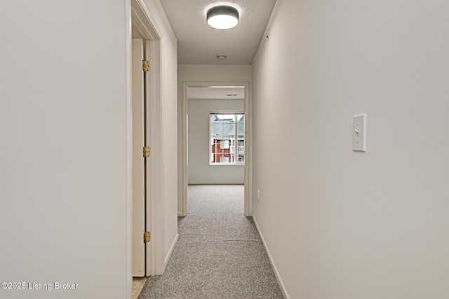 hall with light colored carpet and a textured ceiling